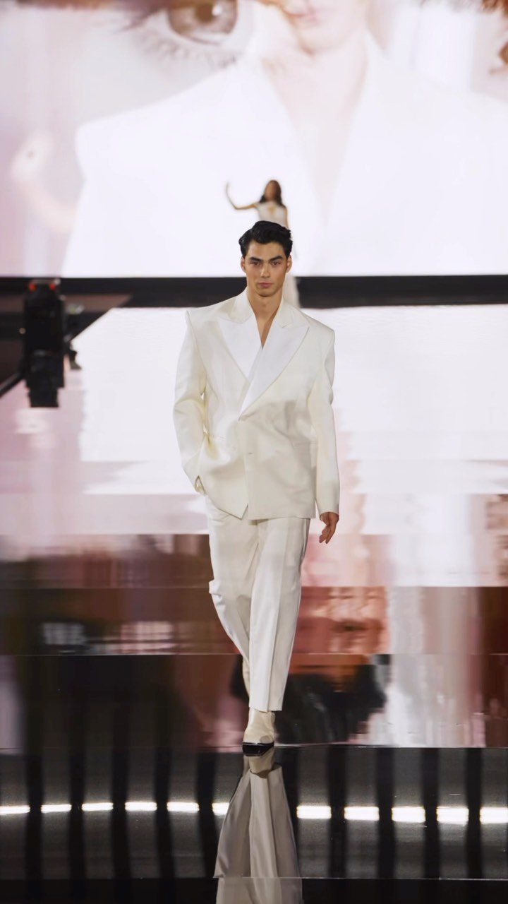 Male model walking a runway in a white double-breasted formal suit.