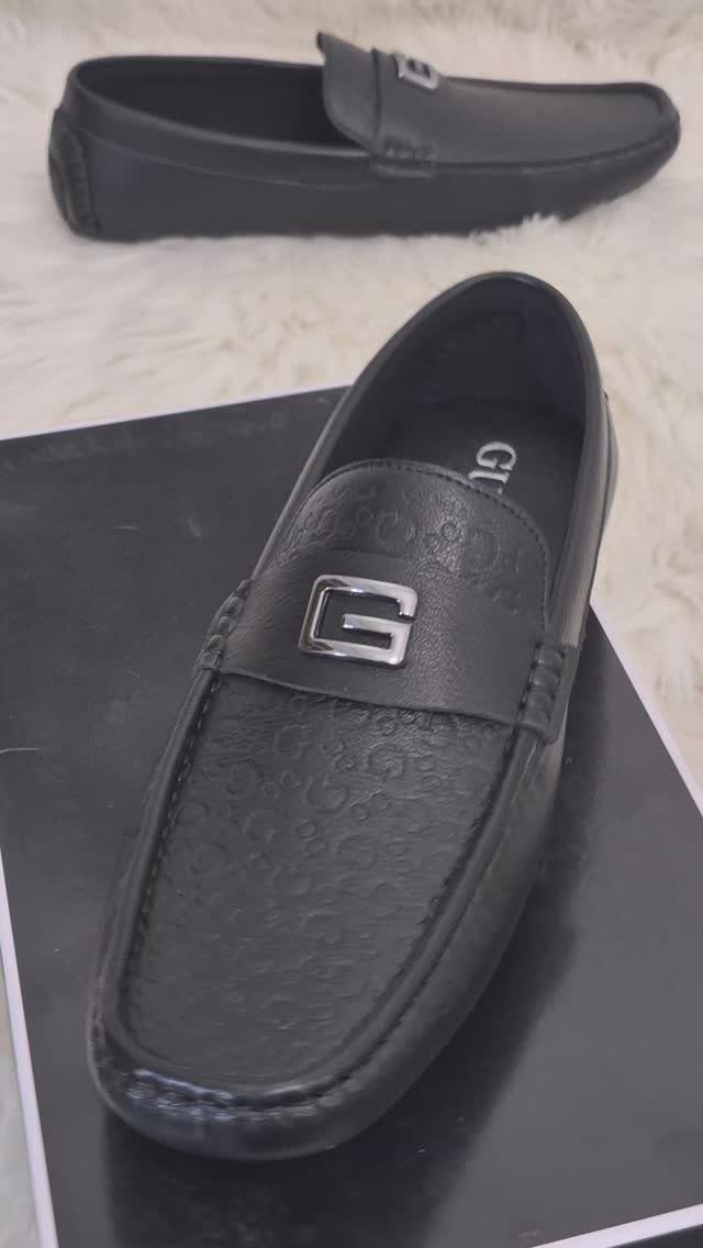 Black leather driving shoes with silver metal emblems resting on a black box and white fur.