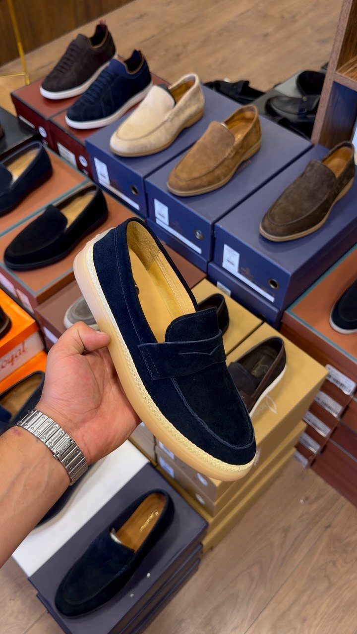 A hand holding a navy blue suede loafer with a thick rope sole in a shoe store.