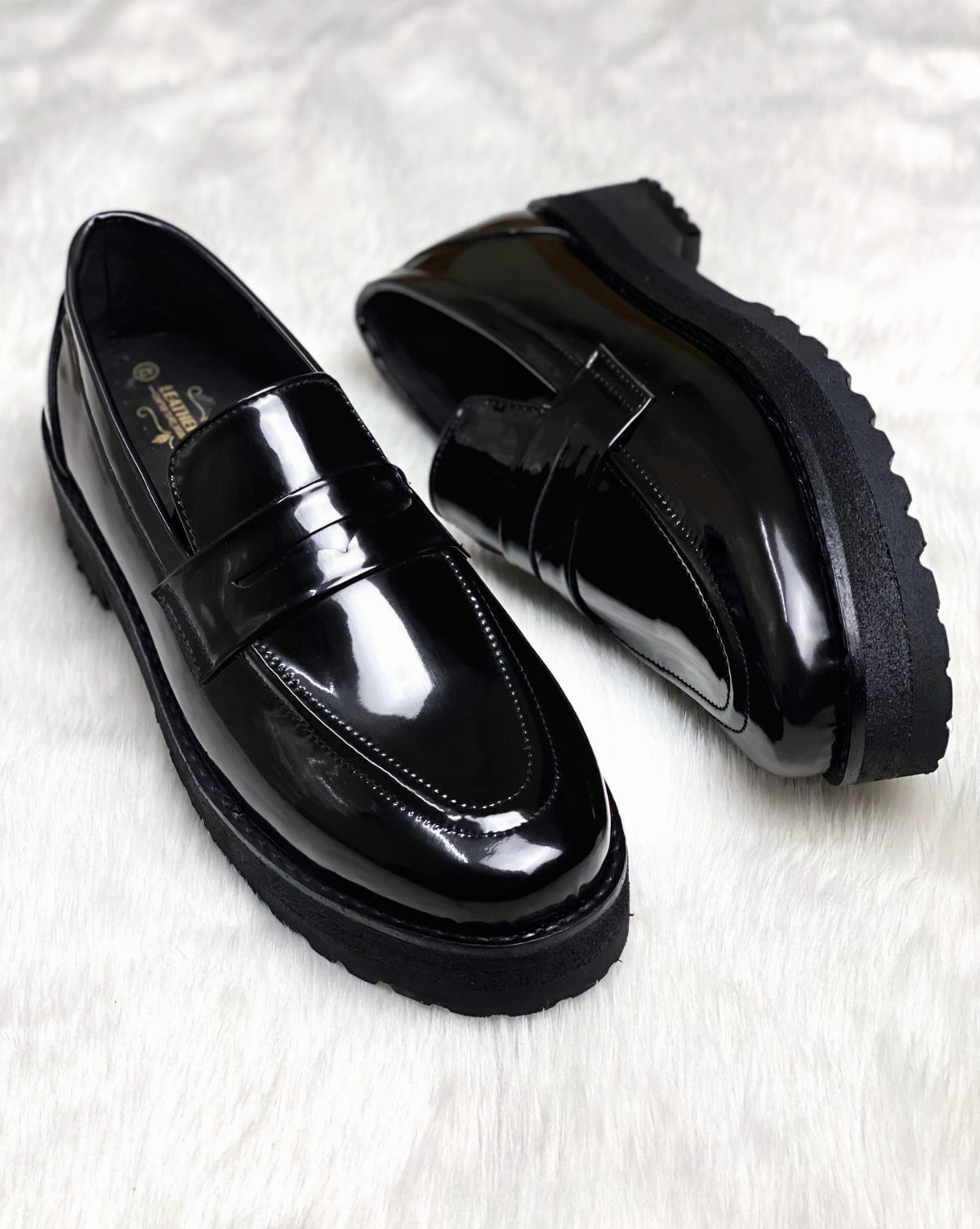 Black patent leather loafers with chunky soles resting on a white textured faux fur background.
