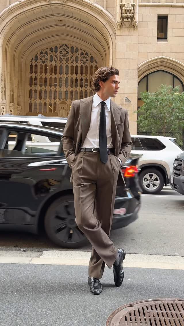 Man in a brown suit and black loafers posing on a city street.