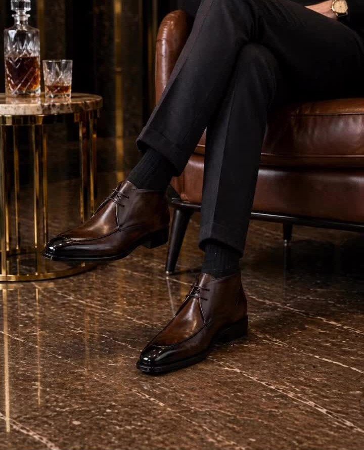 A person wearing dark brown polished leather dress boots and black trousers sitting in a leather chair.