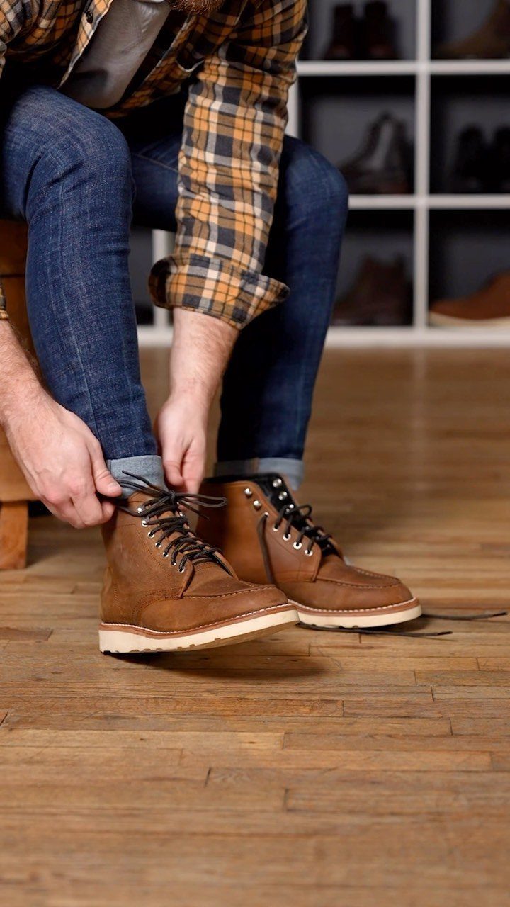 Man tying the laces of his brown leather moc-toe work boots while sitting.