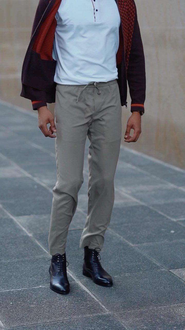 Man wearing tan trousers and black leather lace-up boots standing on a stone walkway.