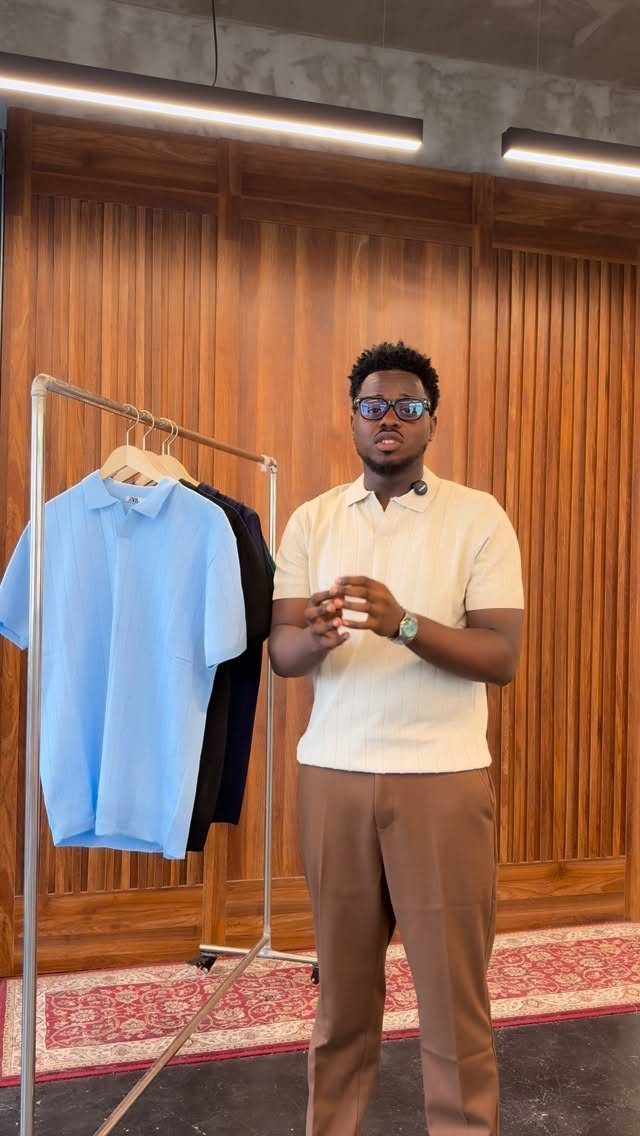 A man in a cream polo shirt and brown trousers standing by a clothing rack.
