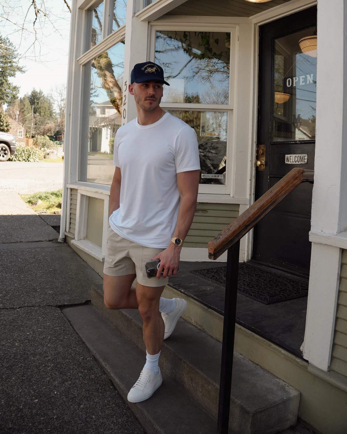 Man in white t-shirt and beige shorts standing on concrete steps outside a building.