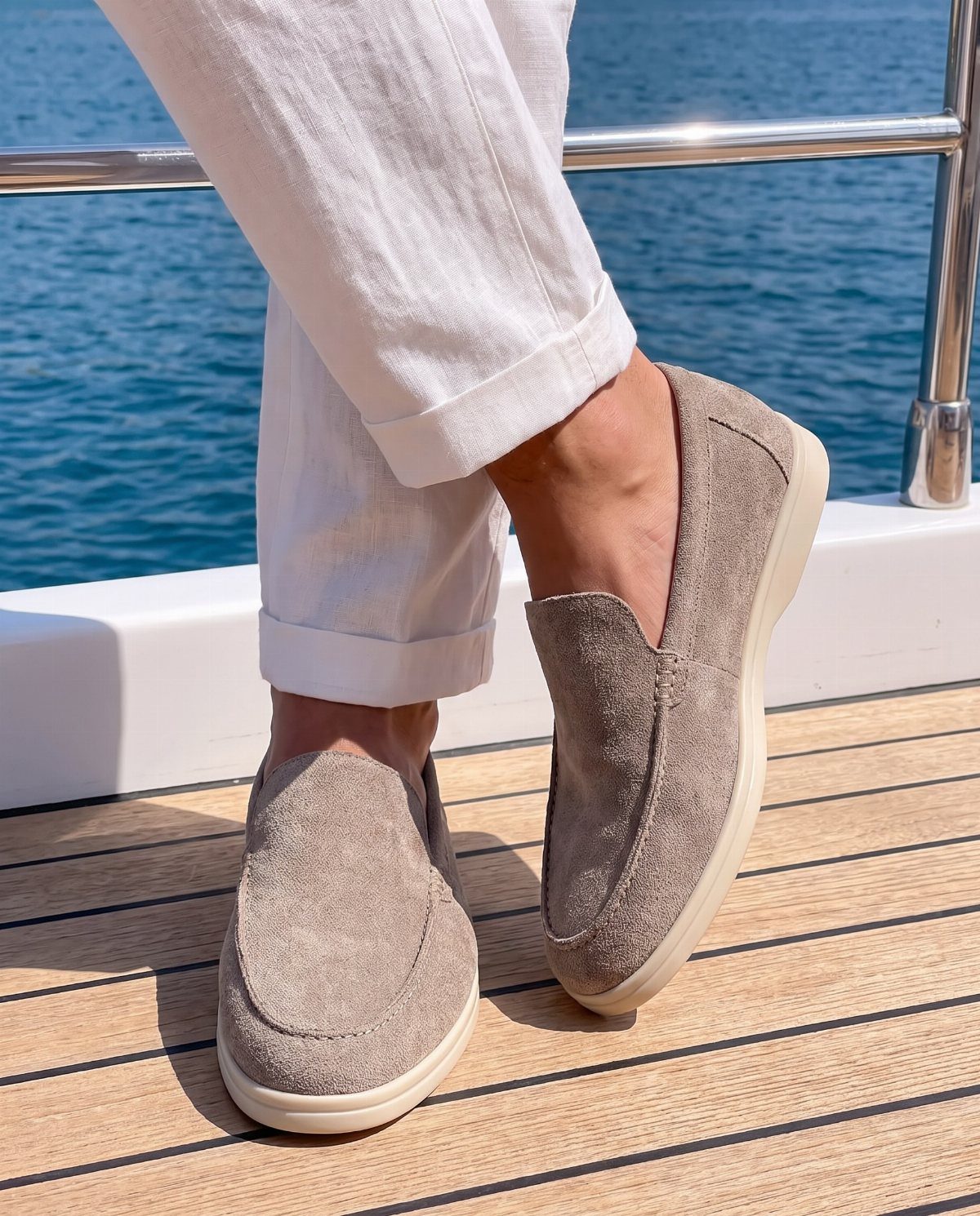 Grey slip-on loafers with white soles worn with white linen trousers on a boat deck.