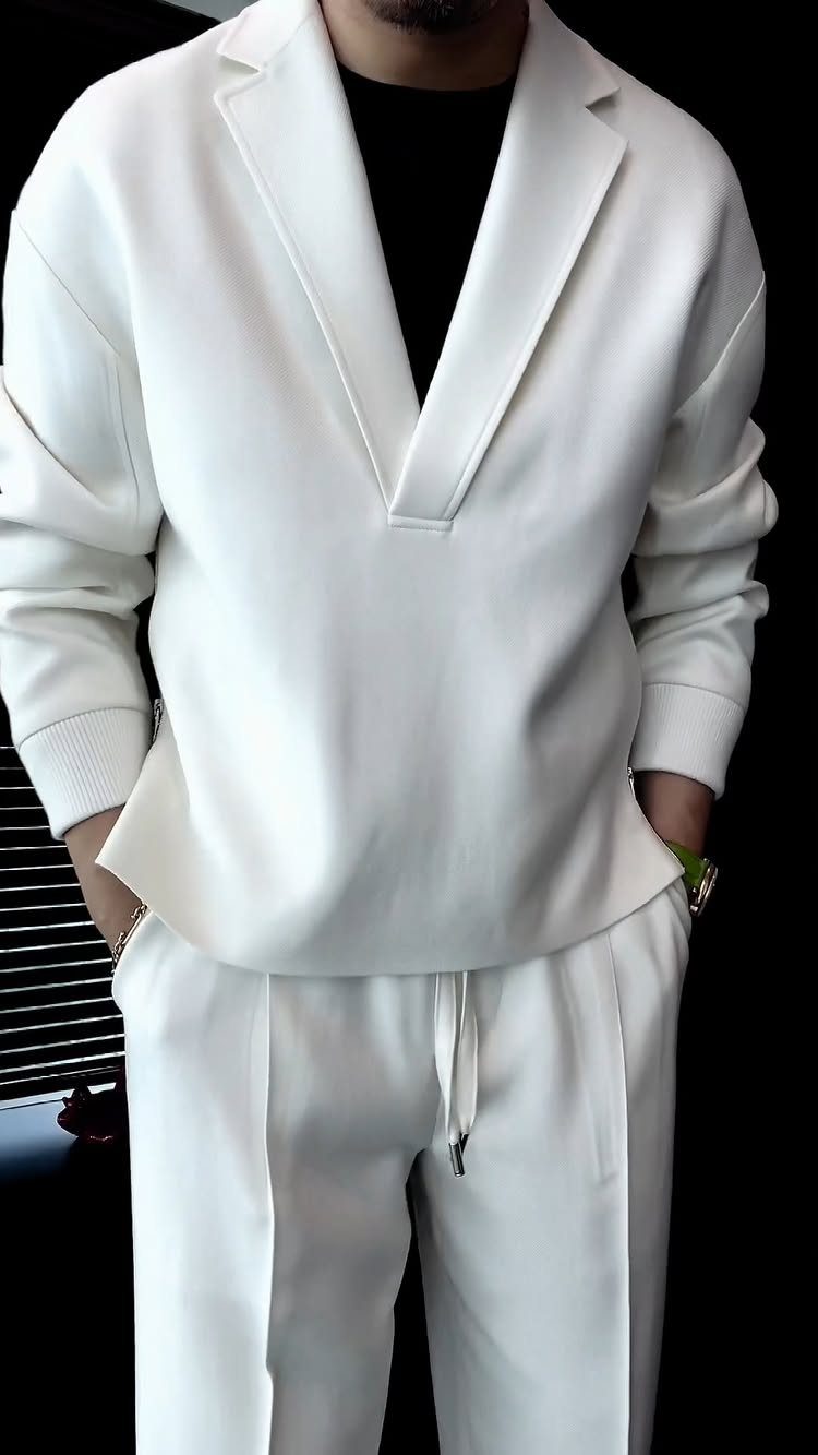 Man wearing a white V-neck blazer top and matching white trousers over a black shirt.