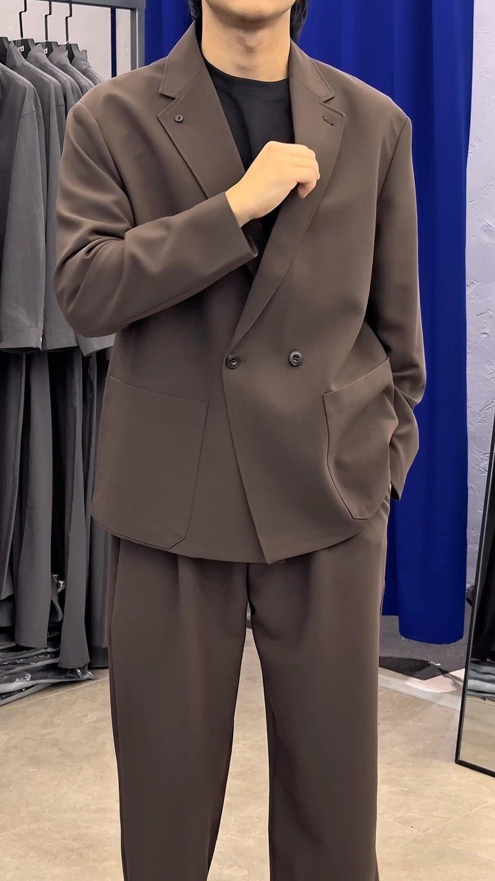 Man wearing a brown double-breasted blazer and matching brown trousers in a clothing store.