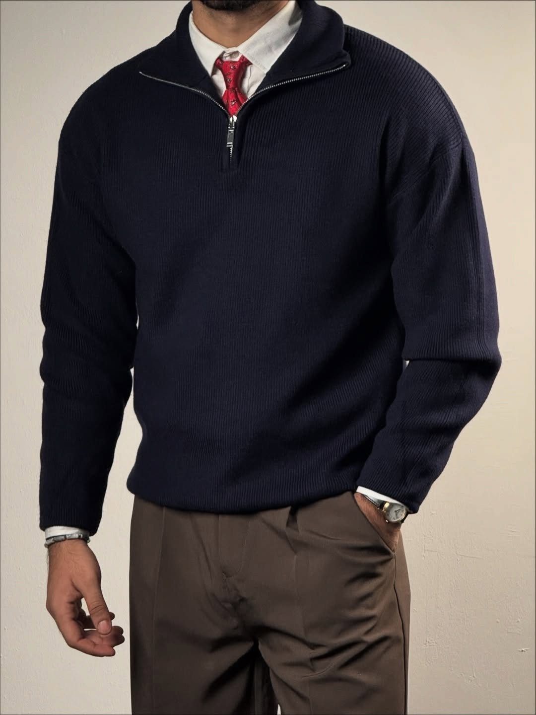 Man wearing a navy quarter-zip sweater, white shirt, red tie, and brown khaki trousers.