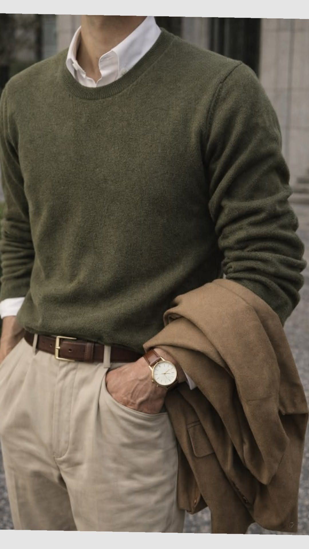 Man dressed in an olive green sweater, white shirt, and beige trousers with a brown leather belt.