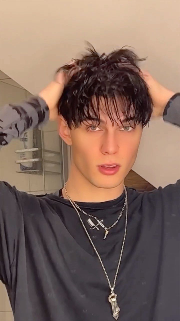 Young man with dark hair running his hands through his messy hair.