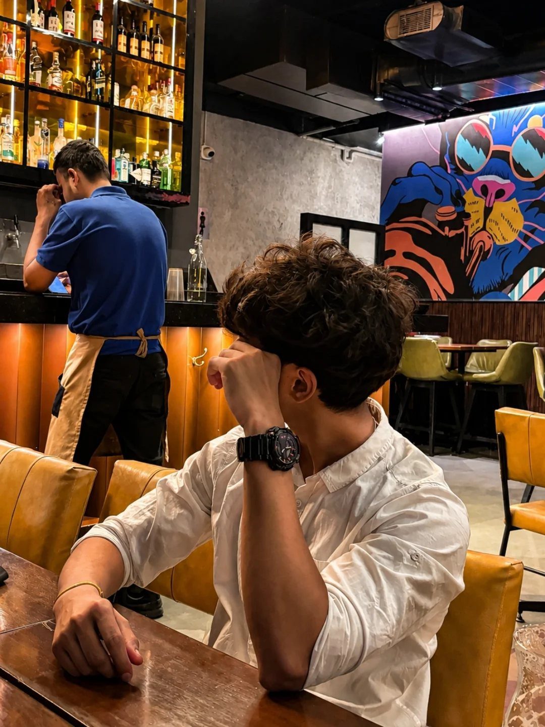 A man in a white shirt rests his chin on his hand while sitting at a table.