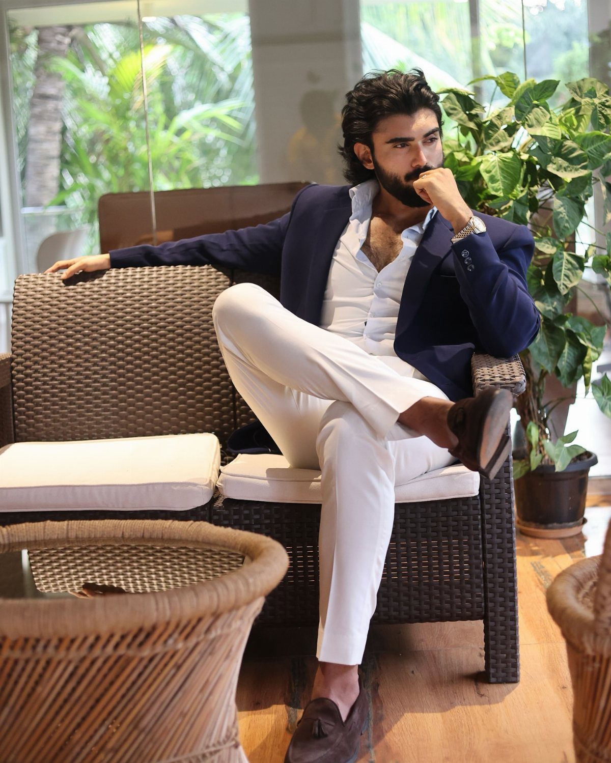 Man in a navy blazer and white trousers reclining on a wicker outdoor sofa.