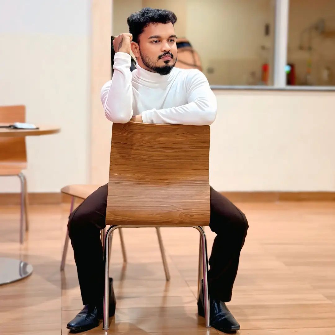 Man in white turtleneck sitting backward on a wooden chair with arms resting on the backrest.