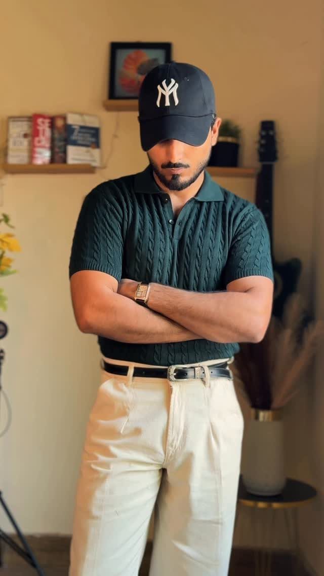 Man in a dark green textured knitted polo shirt and beige trousers posing indoors.