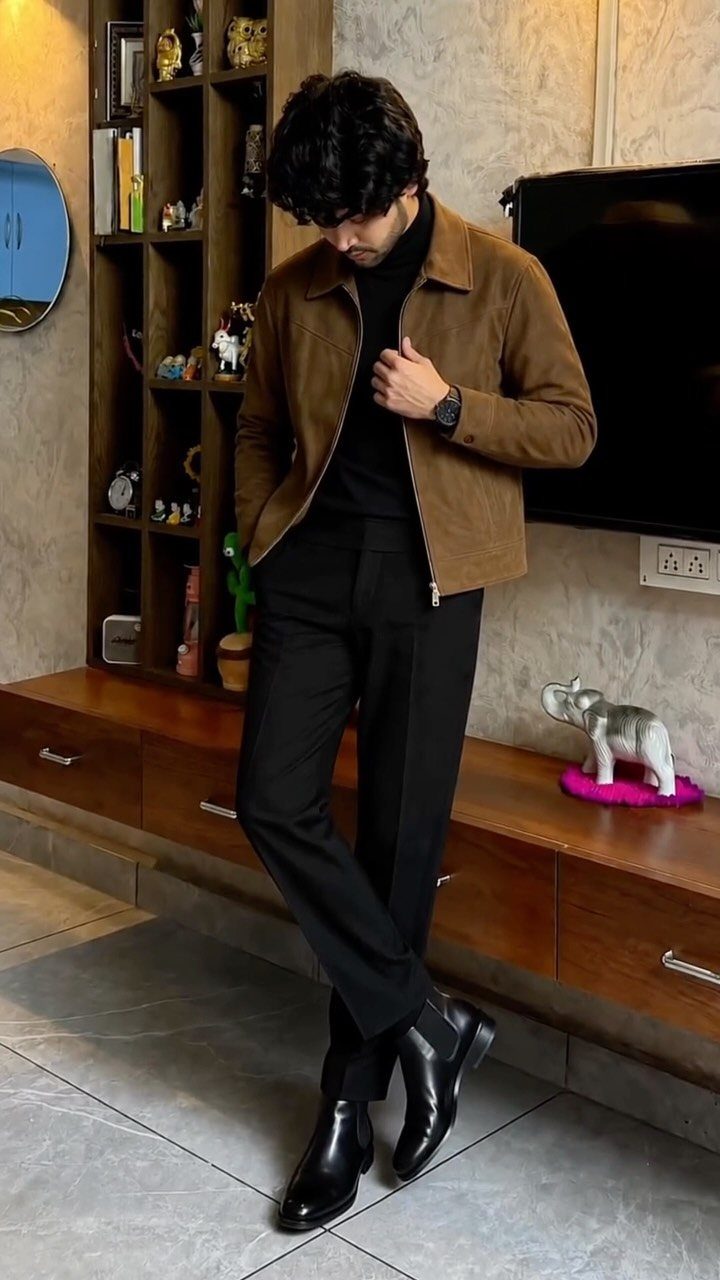 Man wearing a brown suede jacket, black turtleneck, black trousers, and black leather Chelsea boots.