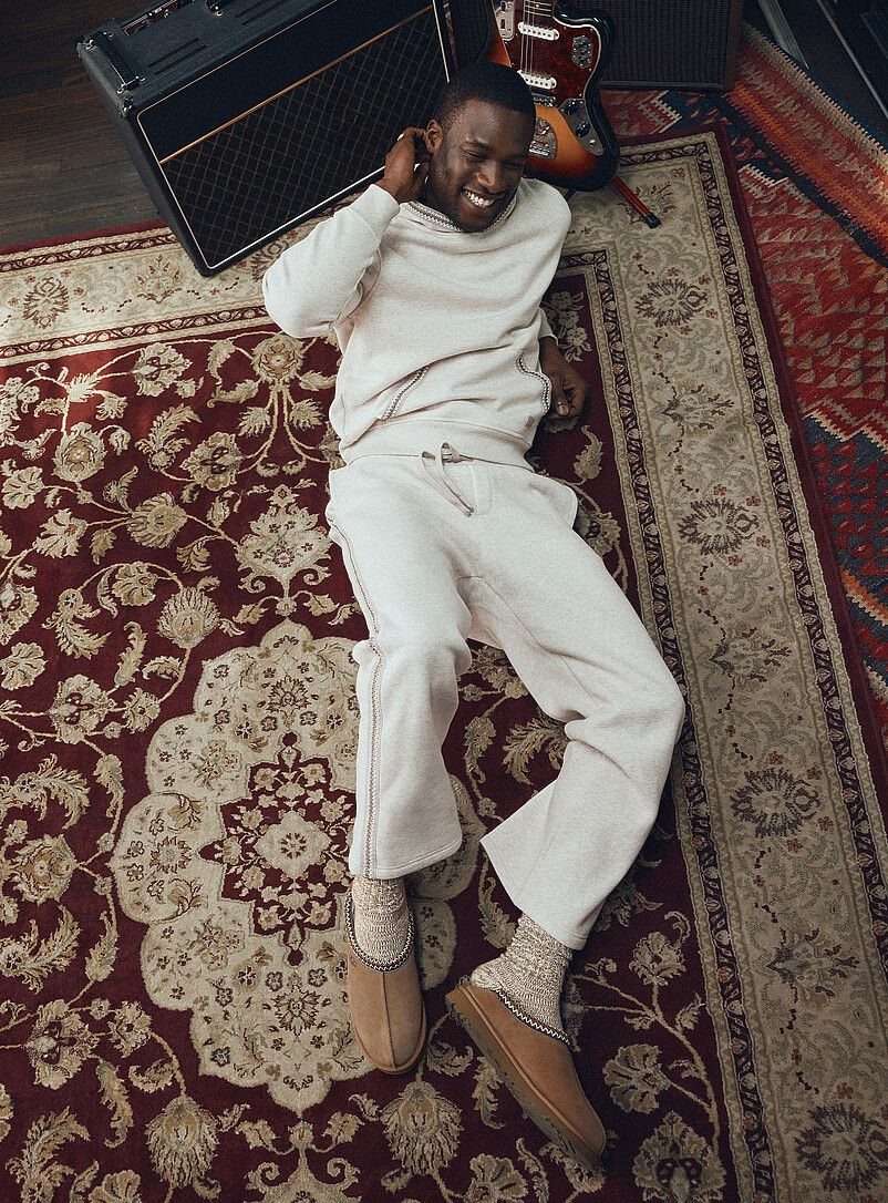 Man in cream loungewear and tan slippers lying on a patterned rug.