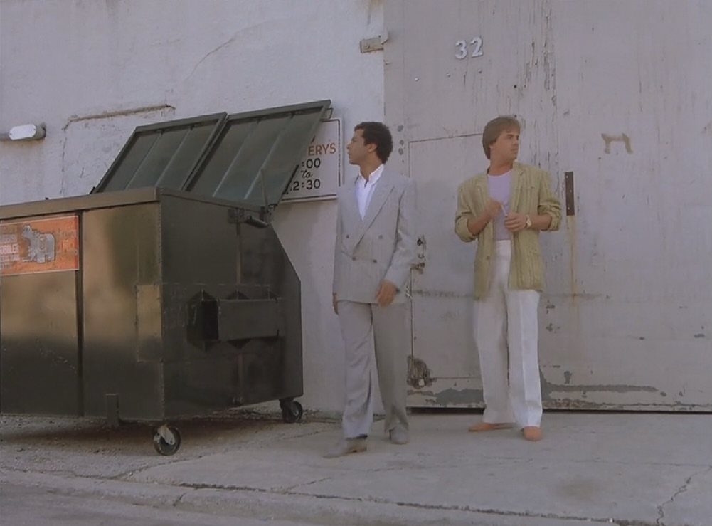 Two men standing in front of a white building wearing pastel colored summer fashion.