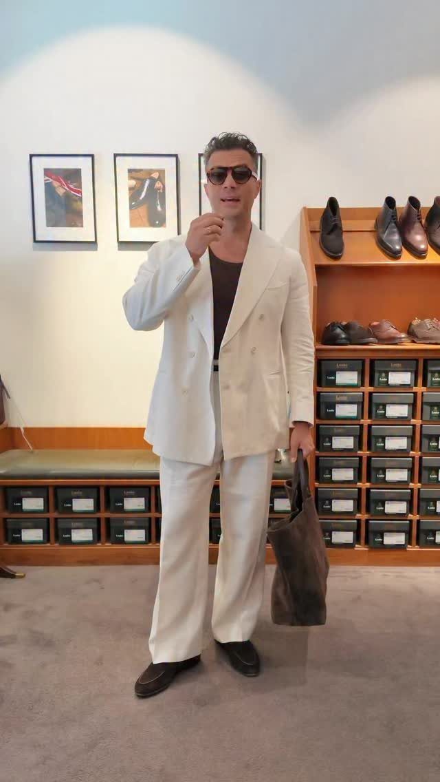 Man in a white suit and dark sunglasses standing in a shoe store.