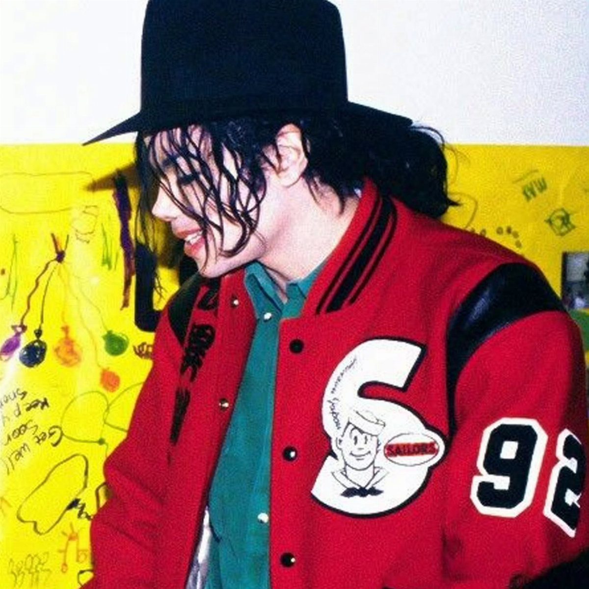 Michael Jackson wearing a black hat and a red varsity jacket with white numbers.