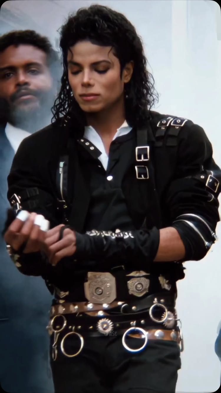 Michael Jackson wearing a black leather jacket decorated with many silver buckles and metal rings.