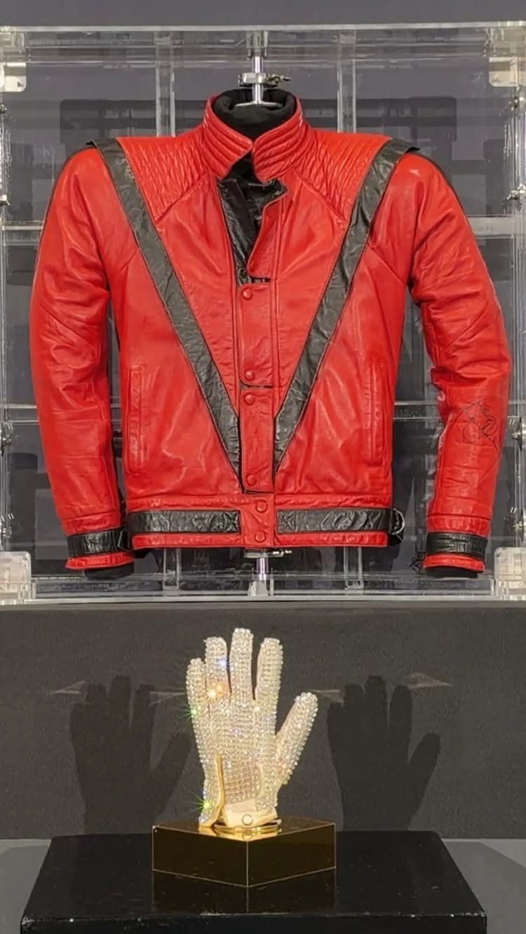 Red leather jacket with black stripes and a white sequined glove on display.