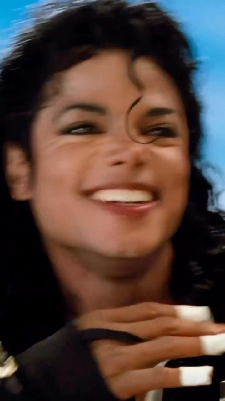 Michael Jackson smiling brightly with dark curly hair against a blue background.