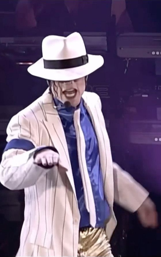 Michael Jackson wearing a white fedora and pinstriped suit while performing on stage.
