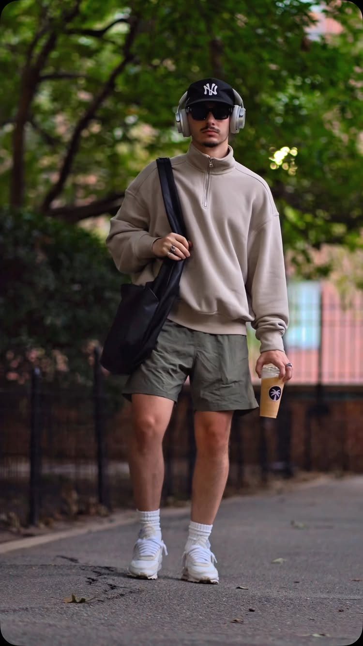 Man in athletic casual wear walking outdoors wearing a beige sweatshirt and olive shorts.
