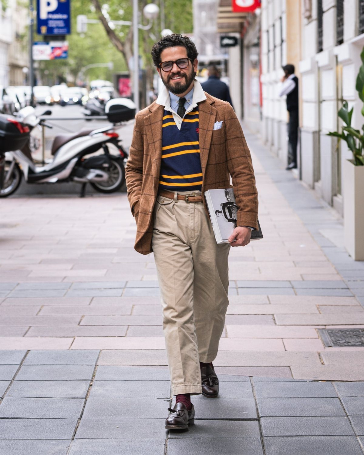 A man in preppy attire walking down a city street carrying a briefcase.