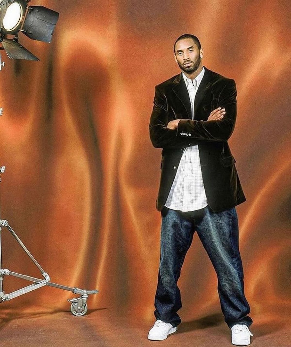 Kobe Bryant posing in a velvet blazer, patterned shirt, and baggy jeans in a studio.