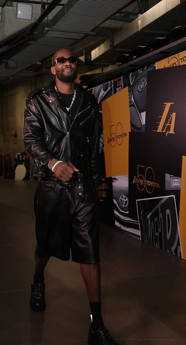 A man posing in a black leather jacket and matching leather shorts with sunglasses.