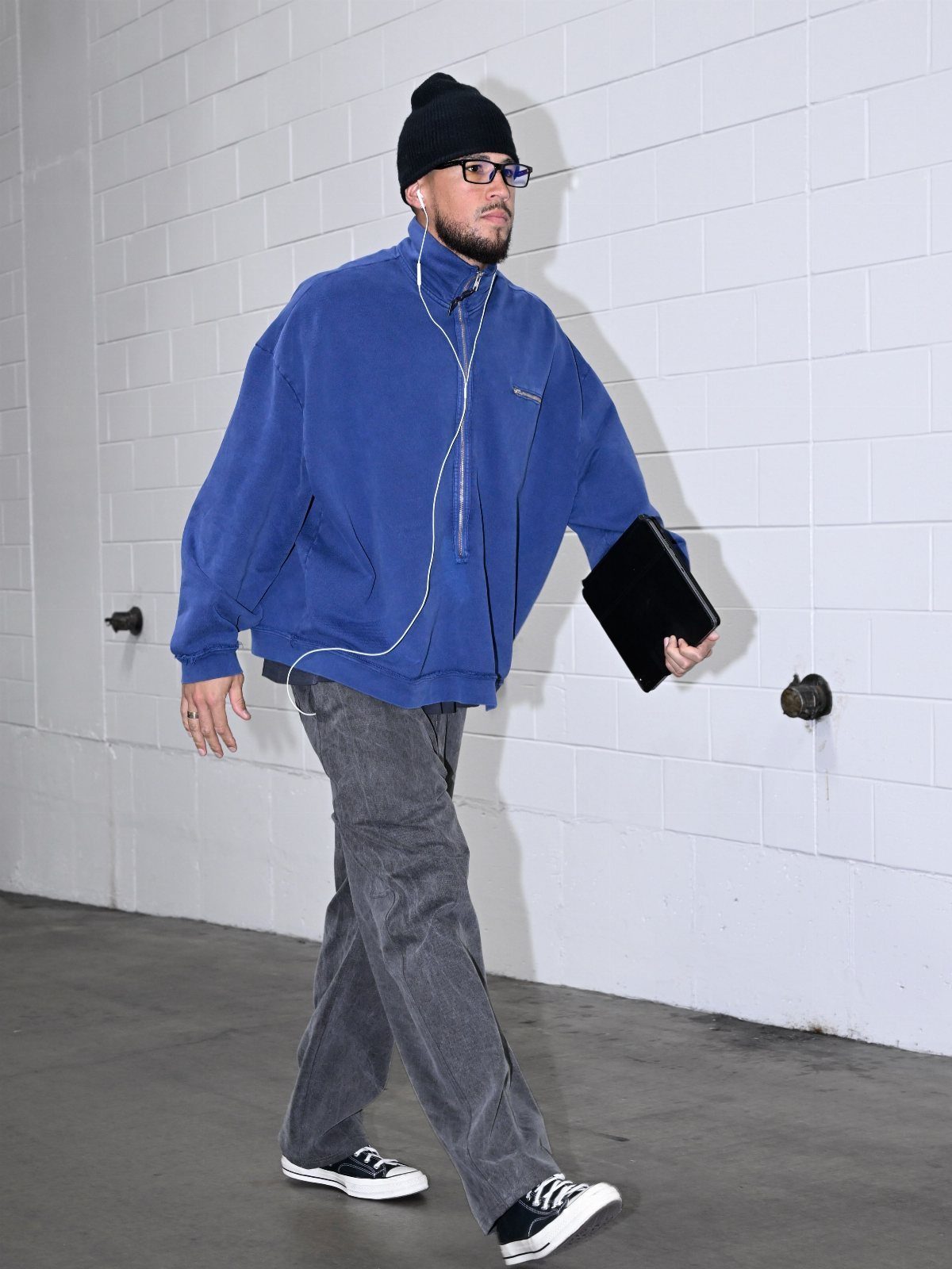 A man in a blue fleece and grey pants walking past a white brick wall.
