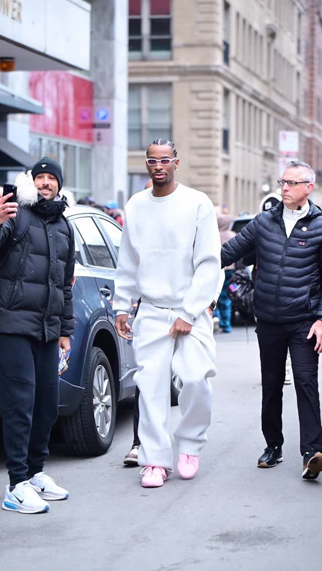 Man in white oversized sweatsuit and pink sneakers walking through a city street.