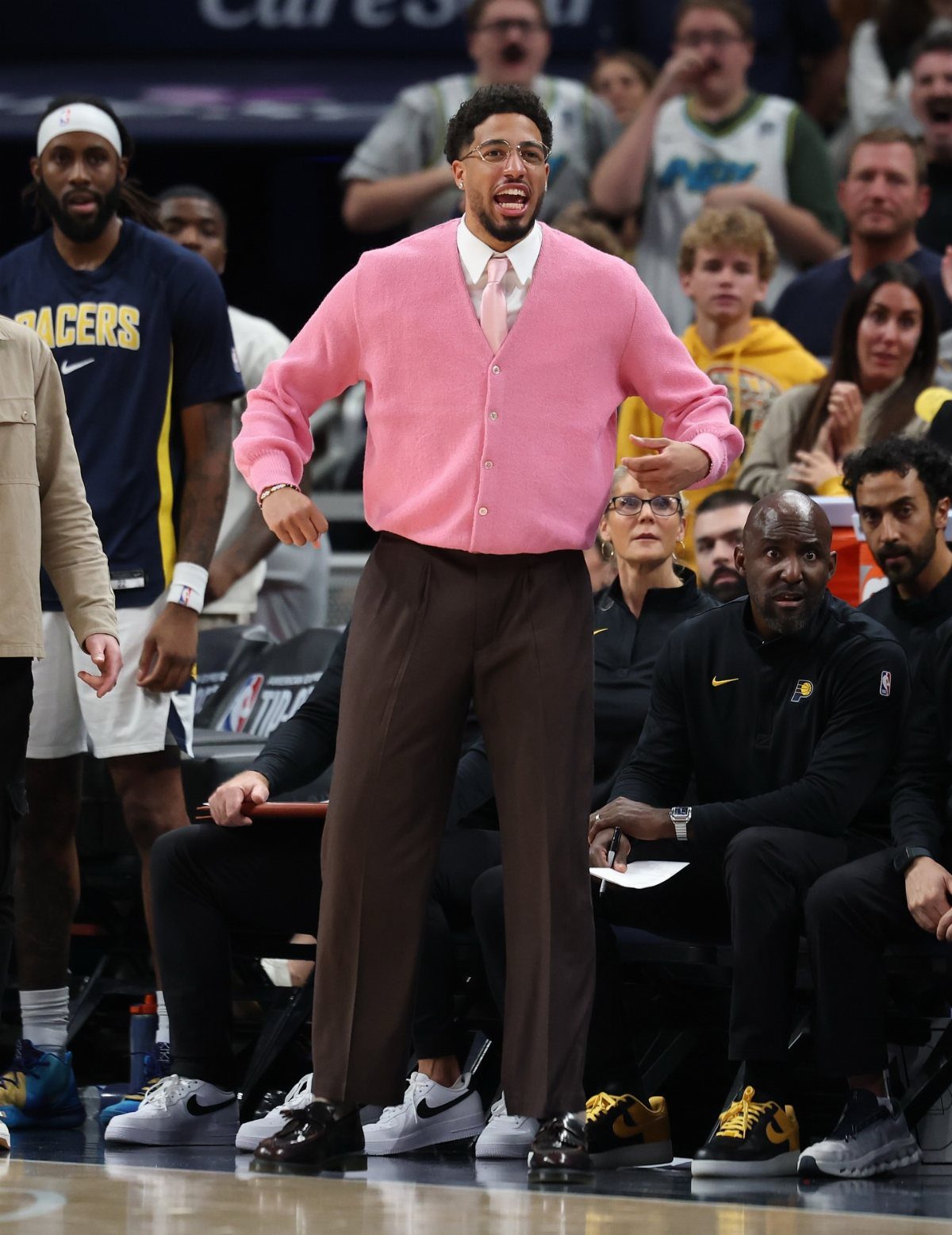 A man in a pink cardigan and brown trousers smiling on a basketball court.