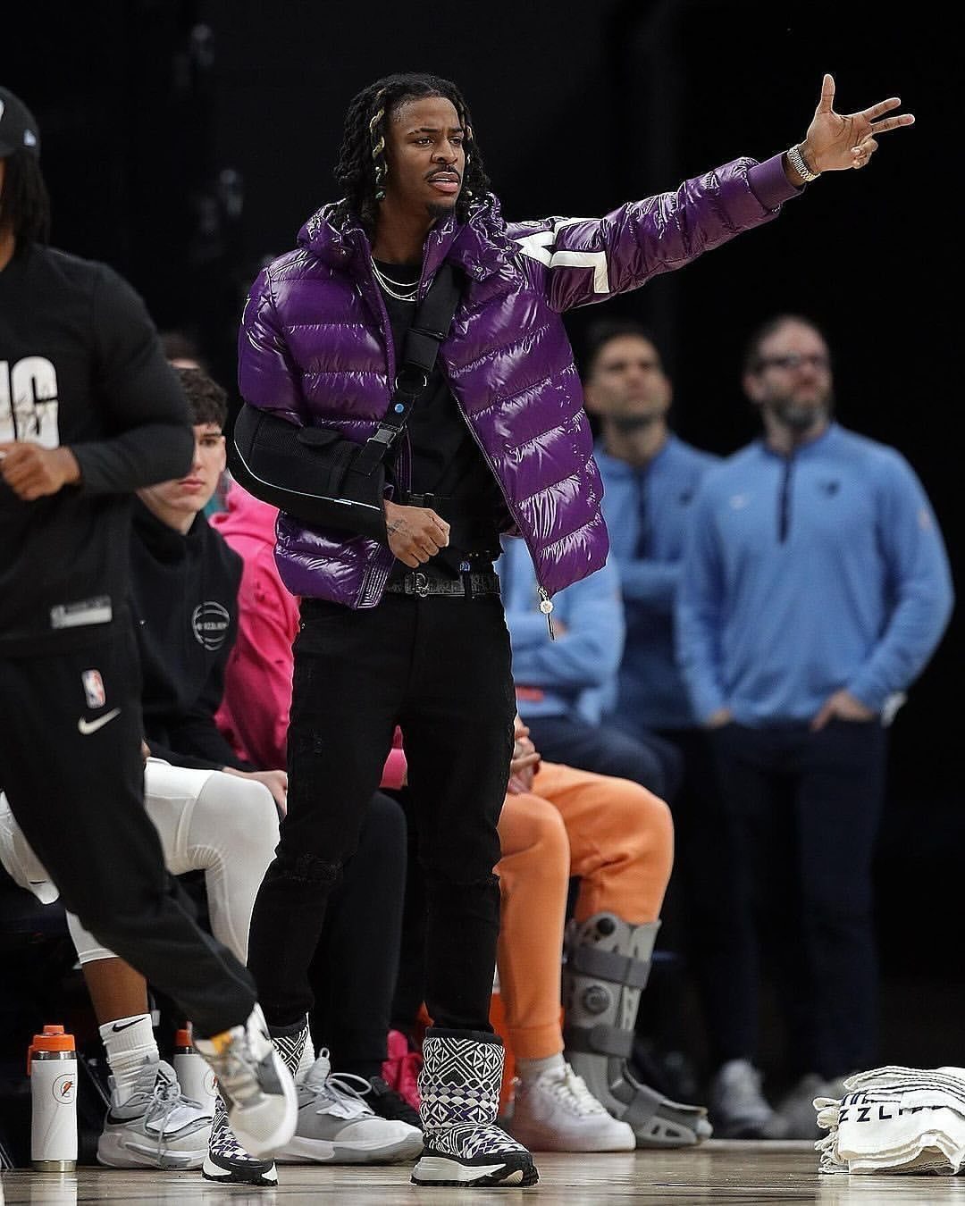 A man in a purple puffer jacket and patterned sneakers gestures on a basketball court.