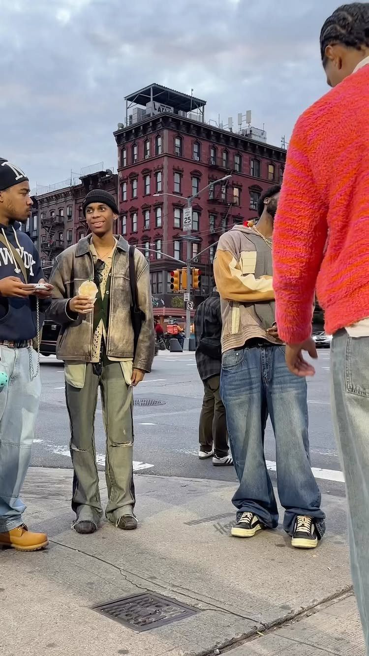 Young men in streetwear standing on a New York City street corner near brick buildings.