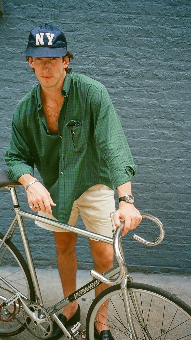 Man in a green shirt and beige shorts standing with a silver bicycle.