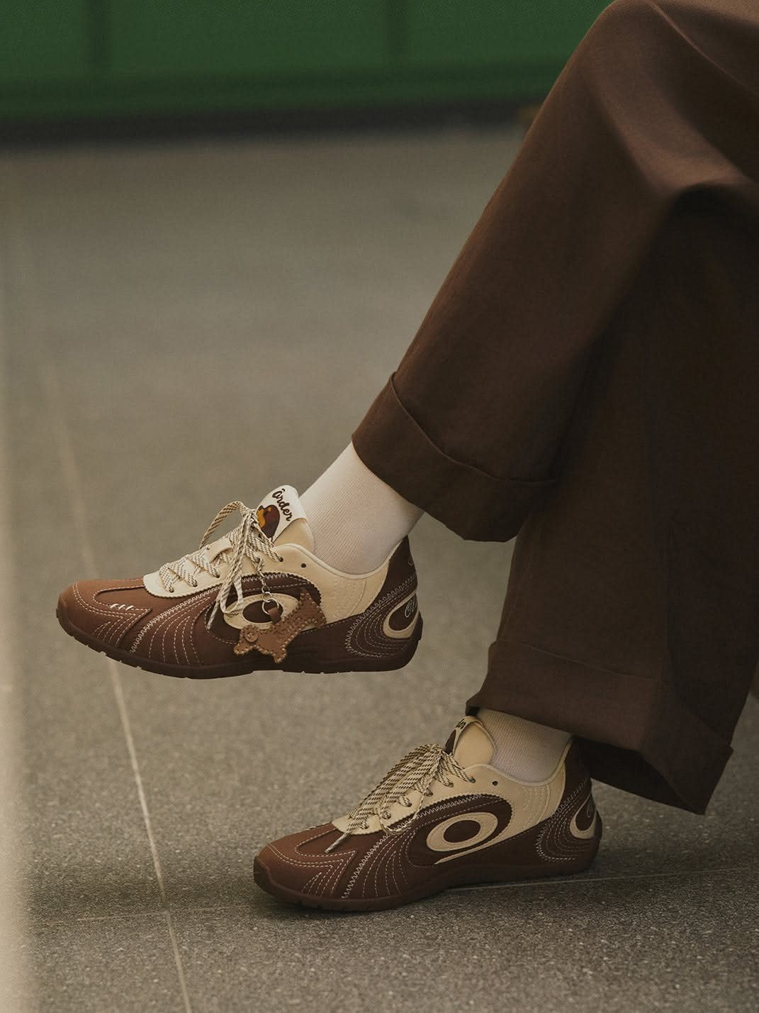 Person wearing brown trousers and cream and brown patterned sneakers with white socks.