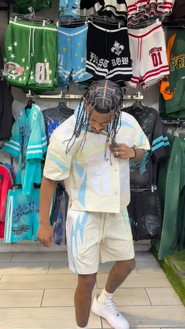 Man wearing a cream and light blue graphic matching shirt and shorts set in a clothing store.