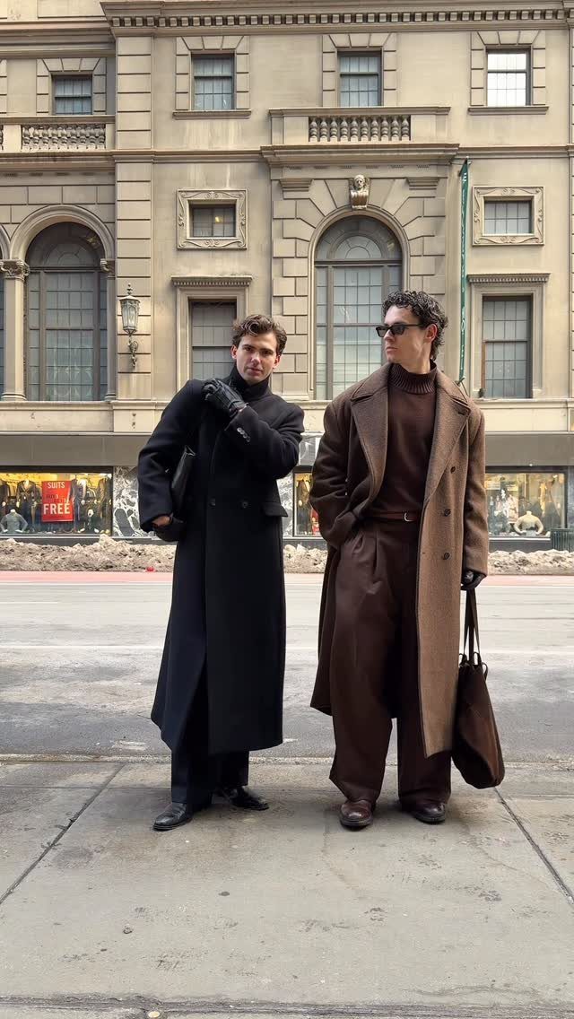 Two men posing in stylish long coats and autumn-colored clothing on a city street.