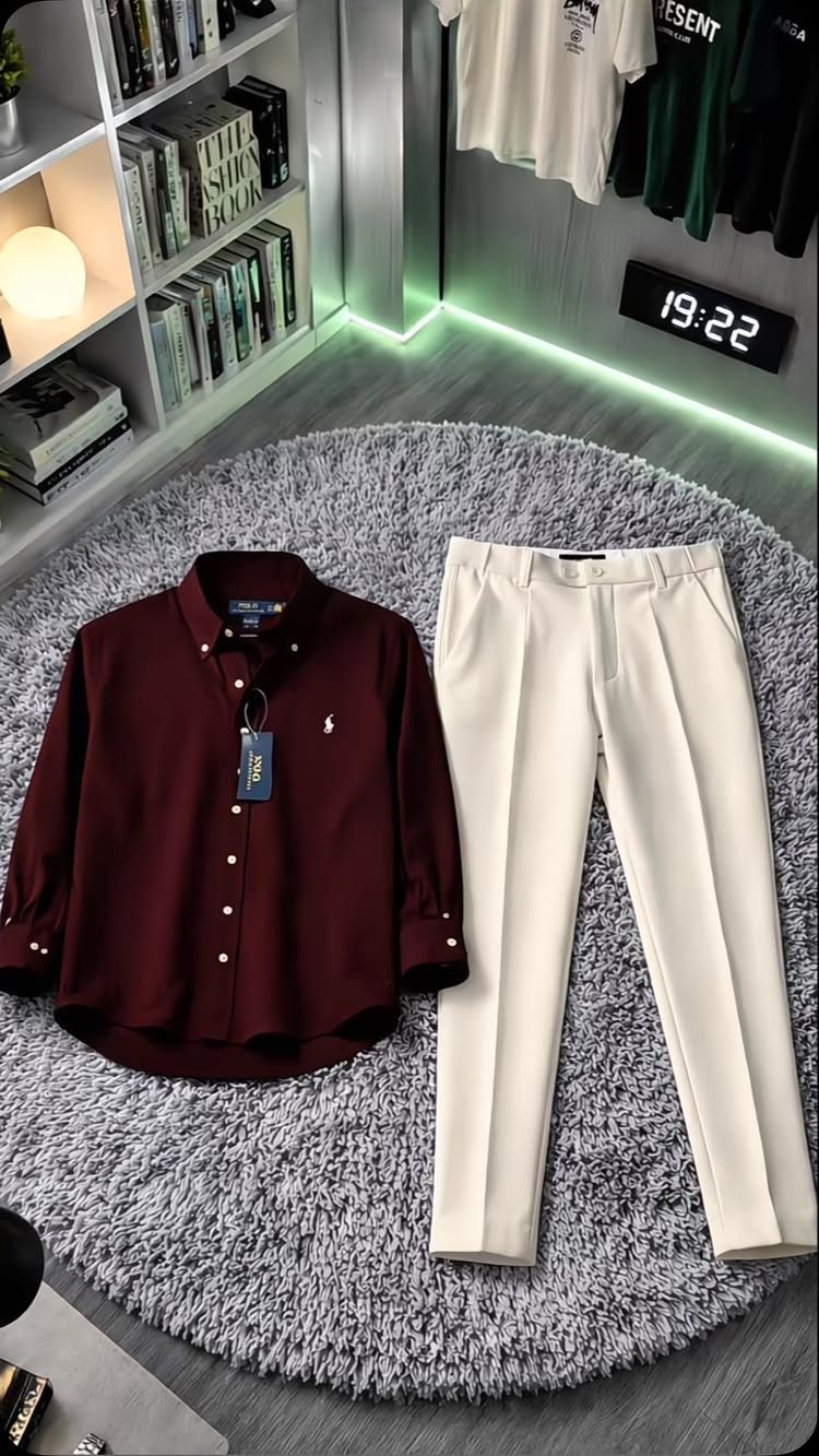 A maroon button-down shirt and cream pleated trousers laid on a grey shaggy rug.