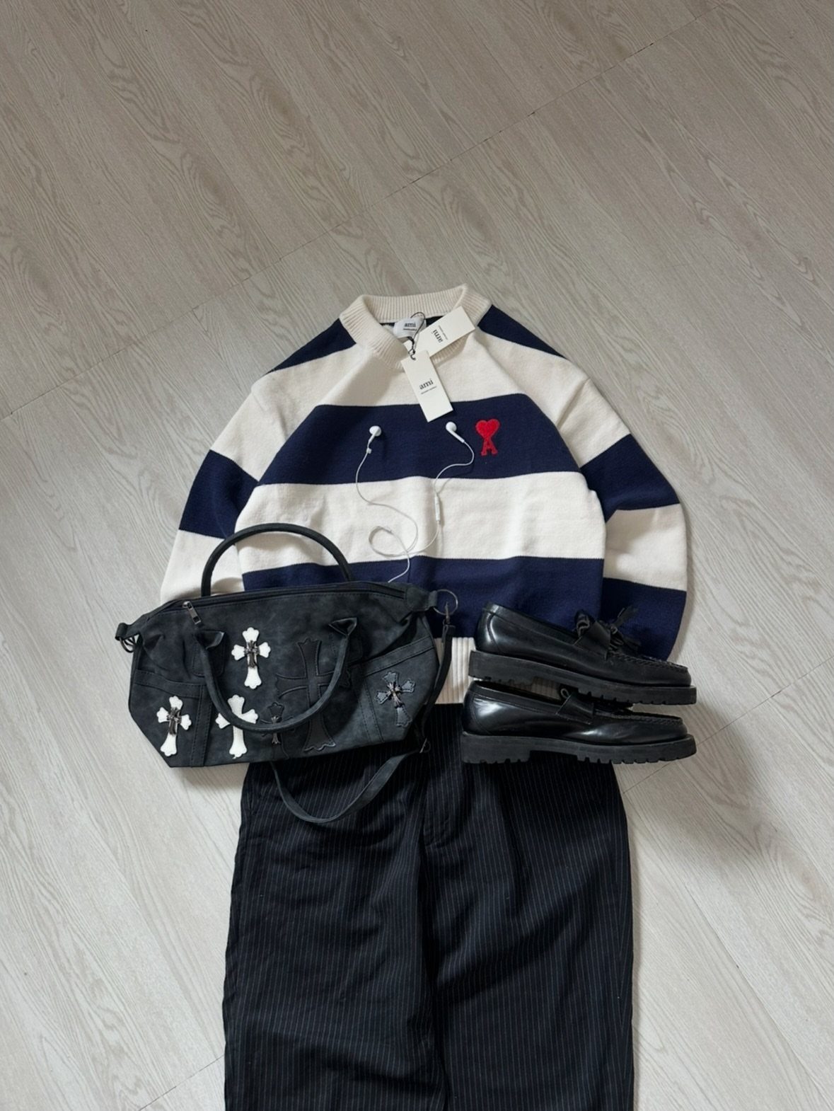Striped navy and white sweater paired with black trousers, loafers, and a black handbag on a wooden floor.