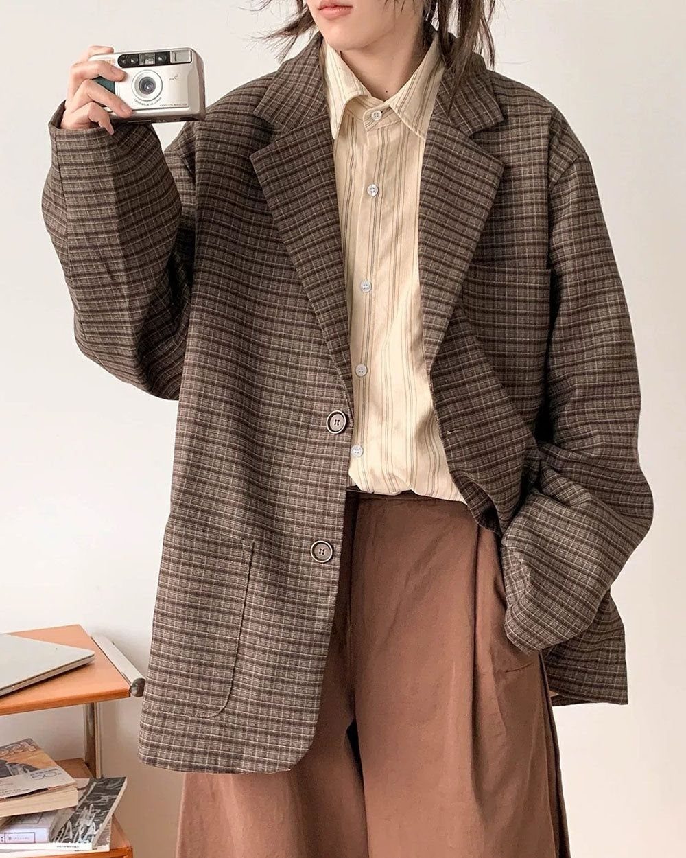 A person wearing an oversized brown plaid blazer, a cream shirt, and brown trousers.