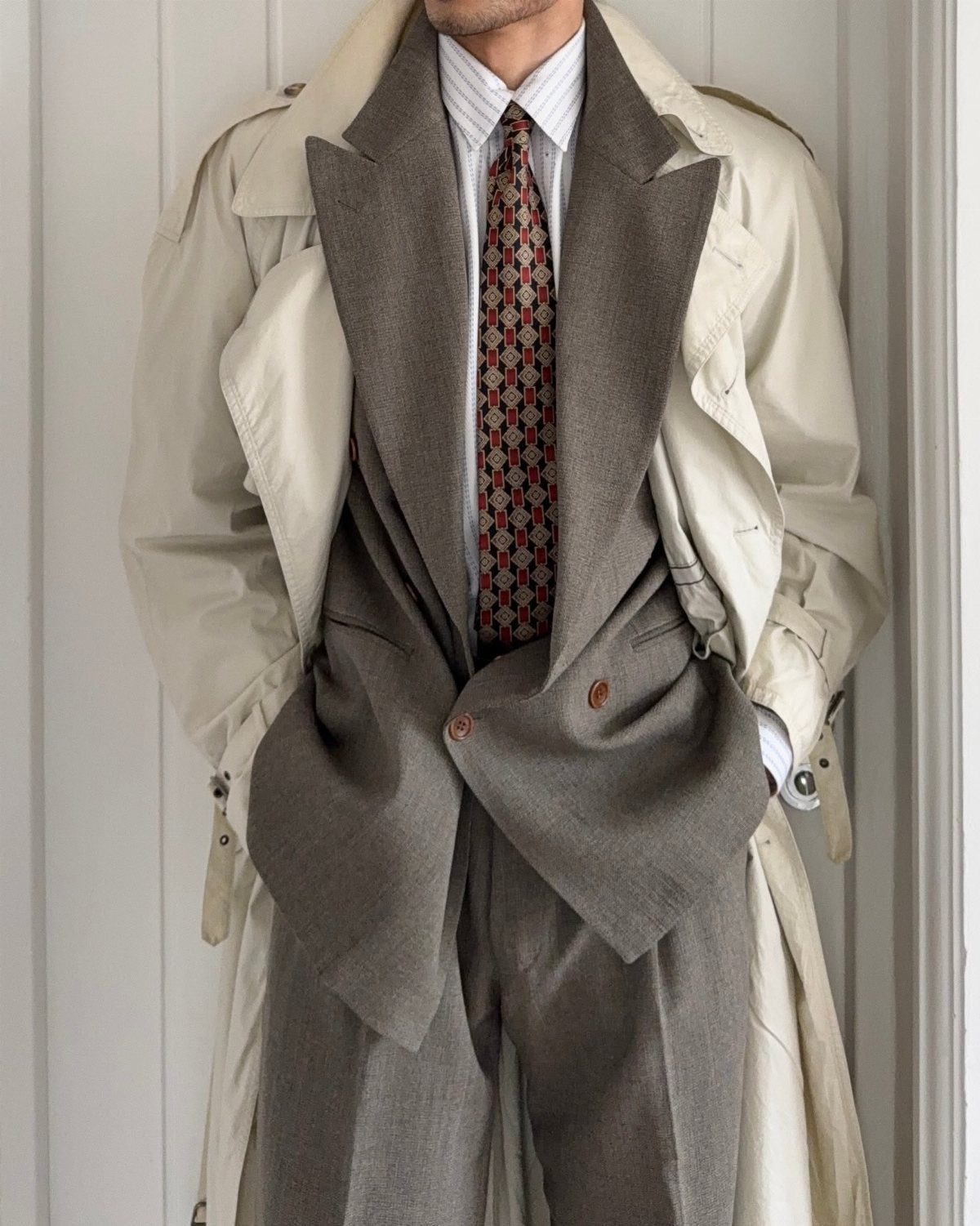 A person wearing a beige trench coat over a grey suit and patterned tie.