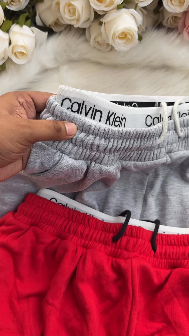 A hand holding the elastic waistbands of grey and red Calvin Klein sweatpants.