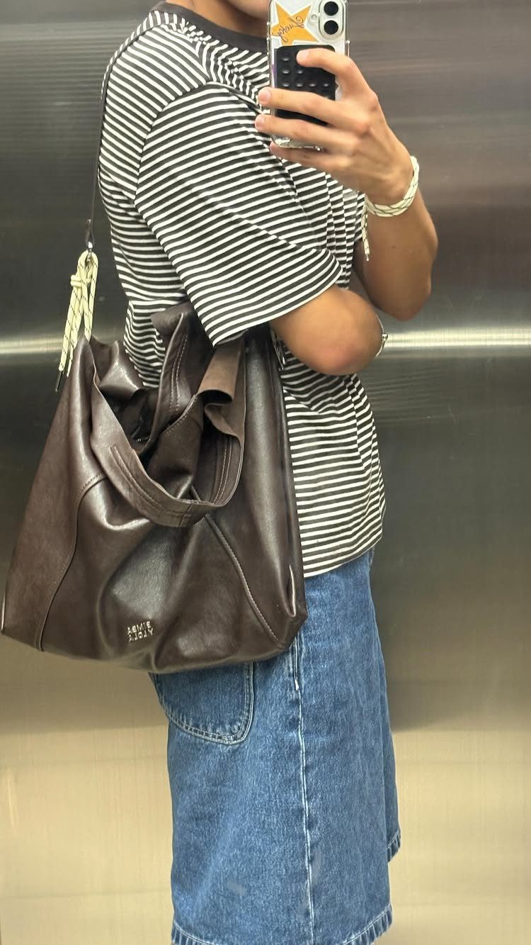 A person in a striped shirt and denim skirt carrying a large brown leather tote bag.