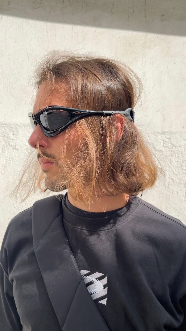 A person with light brown hair wearing black sporty sunglasses and a black sweatshirt.