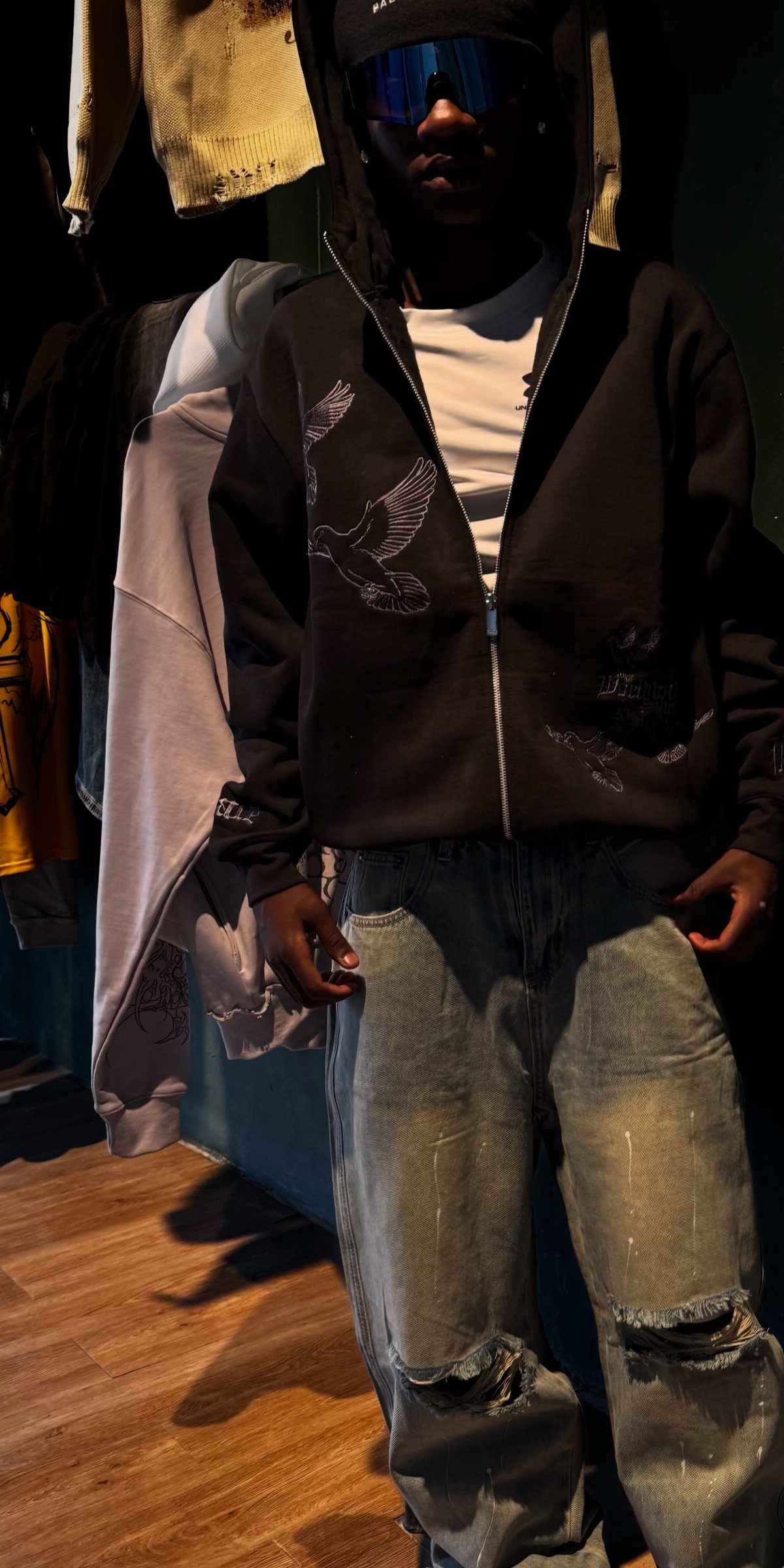 A person wearing a black embroidered hoodie and baggy distressed denim jeans.